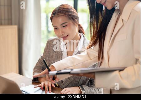 A positive, charming young Asian businesswoman is having a meeting with her colleague, discussing ideas and planning their project. Stock Photo