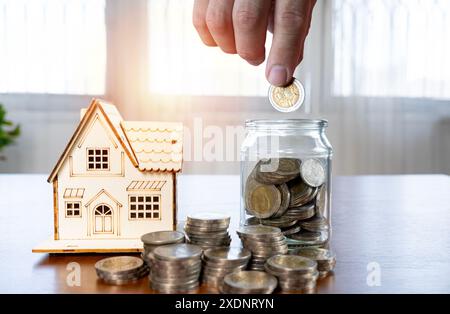 Man Saving Money in a Jar While Calculating Bills at Home, Financial Planning and Budgeting Concept, Close-up of Hand Putting Coin in Glass Jar, Home Stock Photo