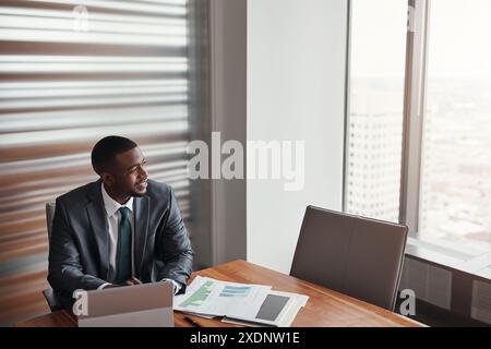 Black man, paperwork and thinking in office on tax, research and plan for growth on laptop. Male person, brainstorming and review credit report for Stock Photo