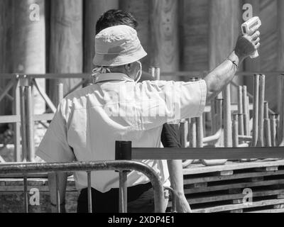 Venice, Italy - June 30th 20220 Security agent wearing a face mask using an infrared thermometer for checking body temperature of a young man Stock Photo