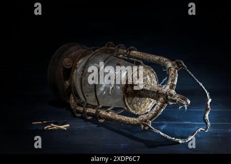 Outdated rusty kerosene lamp and some burnt matches lying on rustic dark blue wood, concept for the hopeless attempt to cling to old tradition and tec Stock Photo
