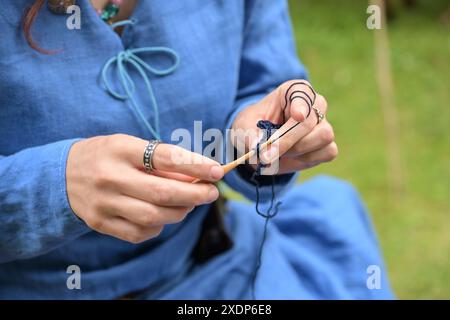 Hands of a young woman in a blue linen dress using a wooden needle to crochet thin wool, copy space, selected focus, narrow depth of field Stock Photo