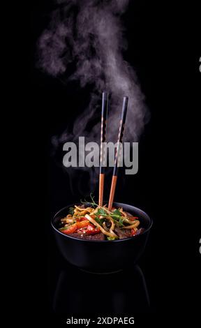 Udon noodles stir-fried with Tiger shrimps and vegetable in wok cooking pan on dark background Stock Photo