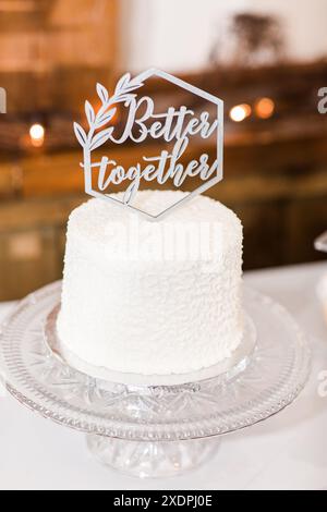 Elegant white wedding cake with "Better Together" sign on glass stand Stock Photo
