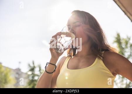 Dehydrated woman drinks clean water from a glass to replenish fluids during hot summer days. Stock Photo