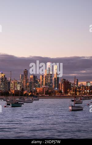 Sunset lit Melbourne skyline over Port Phillip Bay with boats at dusk Stock Photo