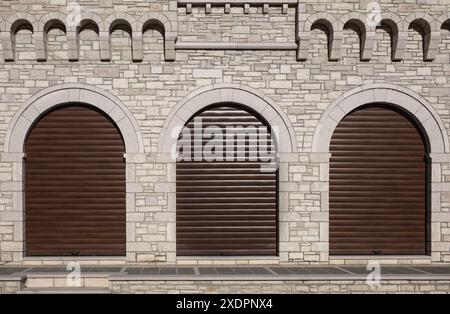 Three loading doors. Rolling metal door of warehouse. Grunge interior background with brick wall and three arched shutter doors. Modern automatic roll Stock Photo