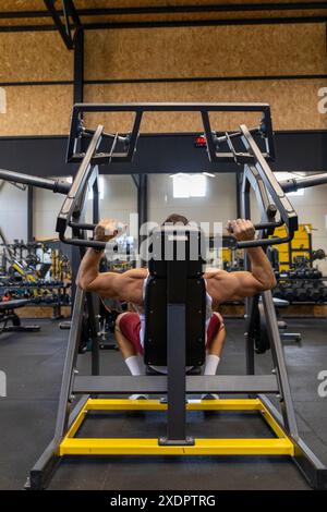 Strong man training shoulders on machine in the gym. Stock Photo