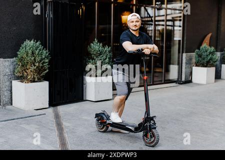 Pleasant smiling man riding a kick scooter. Happy man riding kick scooter Stock Photo