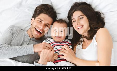 Happy Loving Family Lying In Bed Together Smiling At Camera Stock Photo