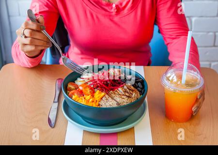 Young girl having quinoa salad with fresh veggies served in a bowl at a healthy cafe restaurant and cold latte. Stock Photo