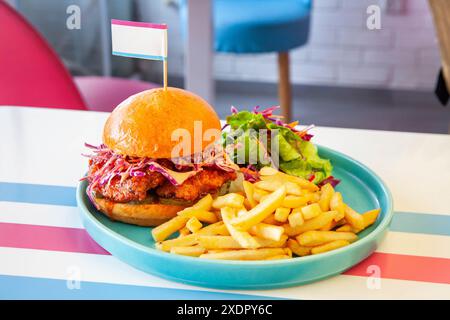 Honey glazed fried chicken burger in brioche bun served with french fries and side salad on a plate in a cafe environment. Stock Photo