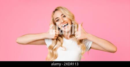 Young Woman Gives Double Thumbs Up Gesture Against Pink Background Stock Photo