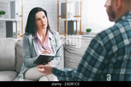 Woman Taking Notes During Therapy Session With Bearded Man Stock Photo
