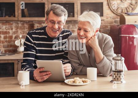 Senior Couple Laughing While Using Tablet Computer in Kitchen Stock Photo