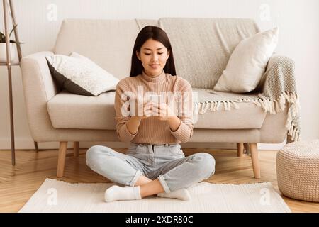 Woman Using Smartphone While Sitting On Floor Stock Photo
