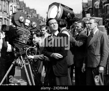 Director DAVID LEAN (centre) and RONALD NEAME (far right) location candid filming street scene for THIS HAPPY BREED 1944 director DAVID LEAN play Noel Coward screen adaptation David Lean Ronald Neame and Anthony Havelock-Allan cinematographer / associate producer Ronald Neame producer Noel Coward Two Cities Films / Noel Coward-Cineguild / Eagle-Lion Distributors Ltd. Stock Photo