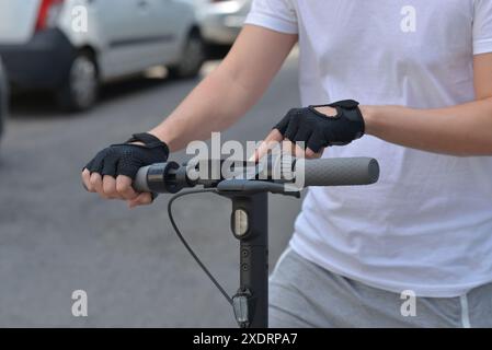 A man wearing black sports gloves turns on an e-scooter by pressing a button. Close up photo. The concept of ecology and healthy lifestyle in the city Stock Photo