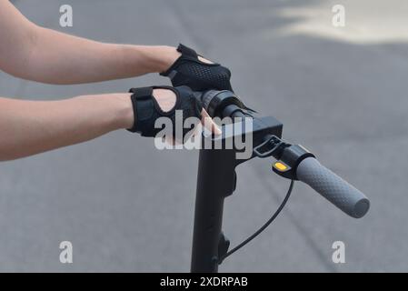 A man wearing black sports gloves turns on an e-scooter by pressing a button. Close up photo. The concept of ecology and healthy lifestyle in the city Stock Photo