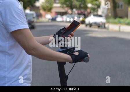 A man on an electric scooter using smartphone. Close up photo of hands in sport gloves. The concept of ecology and healthy lifestyle in the city. Stock Photo