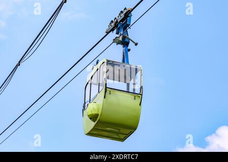 Empty green cabin hanging on cables of cable car against blue sky background, view from a bottom perspective, sunny spring day in Cologne, Germany Stock Photo