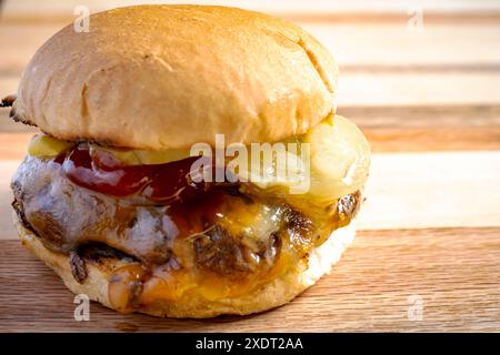 Straight from the grill, burger patty topped with cojack cheese, grilled onions, dill pickles, ketchup and mustard on a toasted bun.   On a wooden boa Stock Photo