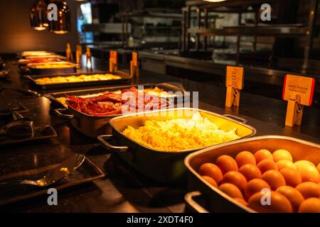 A buffet table with a variety of food, including eggs, omelets, and meat. The table is set in a dimly lit room, creating a cozy and intimate atmospher Stock Photo
