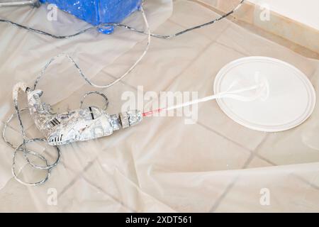 A paint mixer covered with white paint lies on the ground outside a house, indicating ongoing painting work. Stock Photo