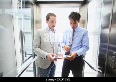 Two executives in elevator, using a digital tablet Stock Photo