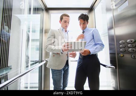 Two executives in elevator, using a digital tablet Stock Photo