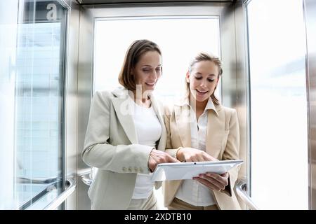 Two executives in elevator, using a digital tablet Stock Photo