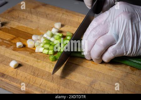 A chef slicing fresh green onions on wooden cutting board. Studio shot Stock Photo