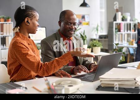 Portrait of senior Black man in business meeting with young colleague in office using laptop computer together Stock Photo