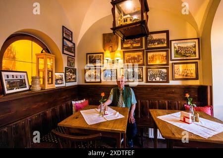An elderly man sits in the dining room of the Gasthof zum Kirchenwirt in Puch bei Hallein, Salzburg, Austria, decorated with historic club photographs. The inn was first documented in the year 1400 and has been family-owned since 1910. Stock Photo