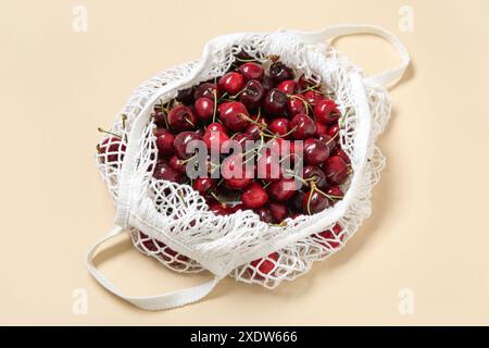 Mesh bag with fresh cherry on beige background, closeup Stock Photo