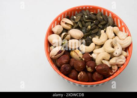 View from above of a bowl filled with a mixture of nuts such as hazelnuts, sunflower seeds, pistachios and cashews in a bowl on isolated white Stock Photo