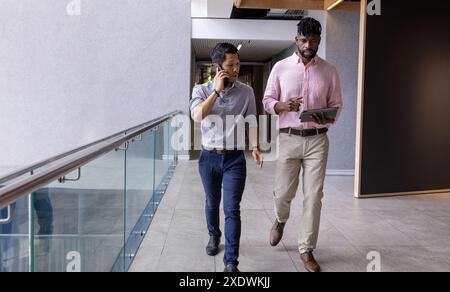 Businessmen walking in office, one talking on phone, other holding tablet Stock Photo