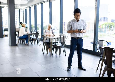 In office, man using smartphone while colleagues working at tables in background Stock Photo