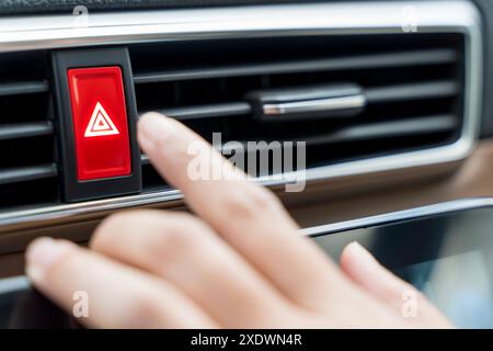 The driver is pressing the emergency stop button on the car dashboard. while stopping the car suddenly. Finger pushing warning light in car. Stock Photo