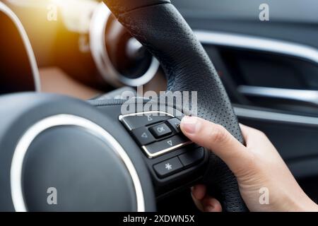 Woman's hand presses the button on the steering wheel of the car close-up. Multi function buttons on steering wheel in car. Back view of woman driver Stock Photo