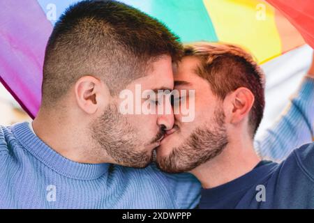Gay male couple kissing under rainbow lgbtq flag during pride month parade. Love relationship concept Stock Photo