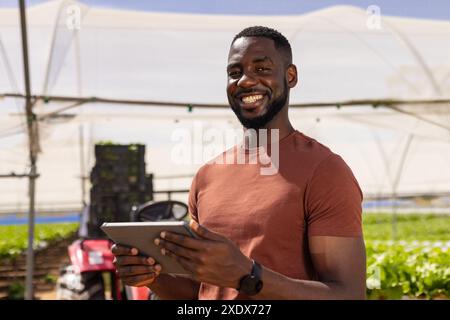 African American farmer using tablet for managing hydroponic farm, smiling outdoors Stock Photo