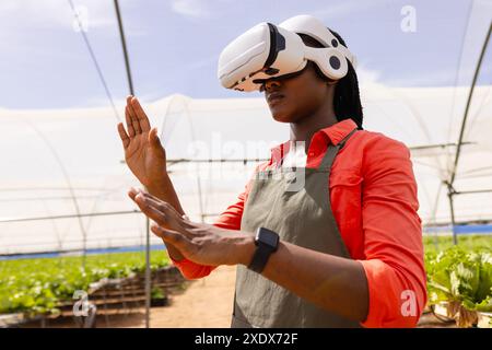 Using VR headset, farmer in apron managing hydroponic farm in greenhouse Stock Photo