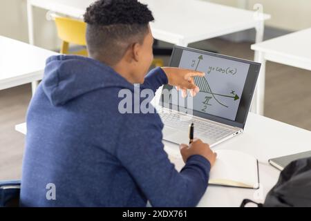 In school, male student pointing at graph on laptop screen while taking notes Stock Photo
