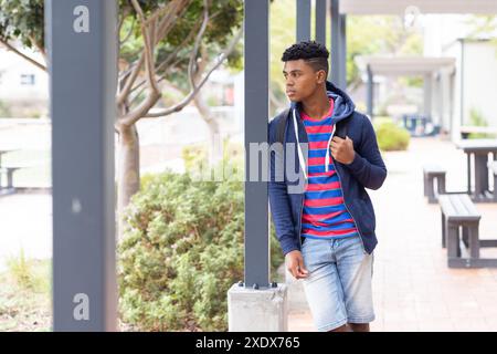 Walking outdoors, African American male student wearing backpack, looking away thoughtfully, copy sp Stock Photo