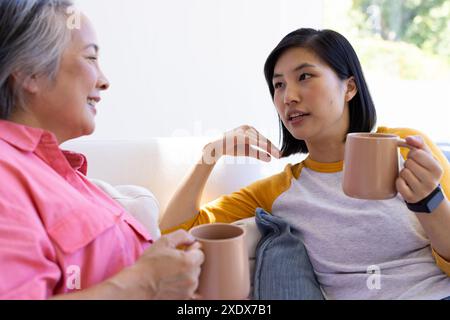 Asian woman and senior woman drinking coffee, having conversation on sofa Stock Photo