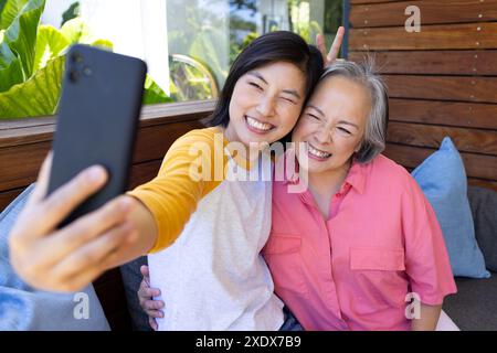 Taking selfie, Asian woman and senior woman smiling together on couch Stock Photo