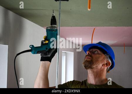 Construction worker wearing protective gear using power drill to install drywall on ceiling in new home construction. Stock Photo