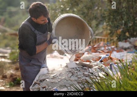 Construction worker emptying debris from carrycot in a container Stock Photo
