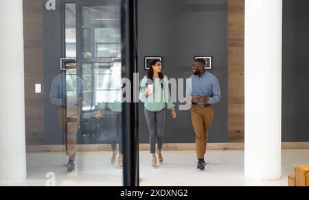 Walking in office, diverse business colleagues discussing work, holding coffee cup Stock Photo